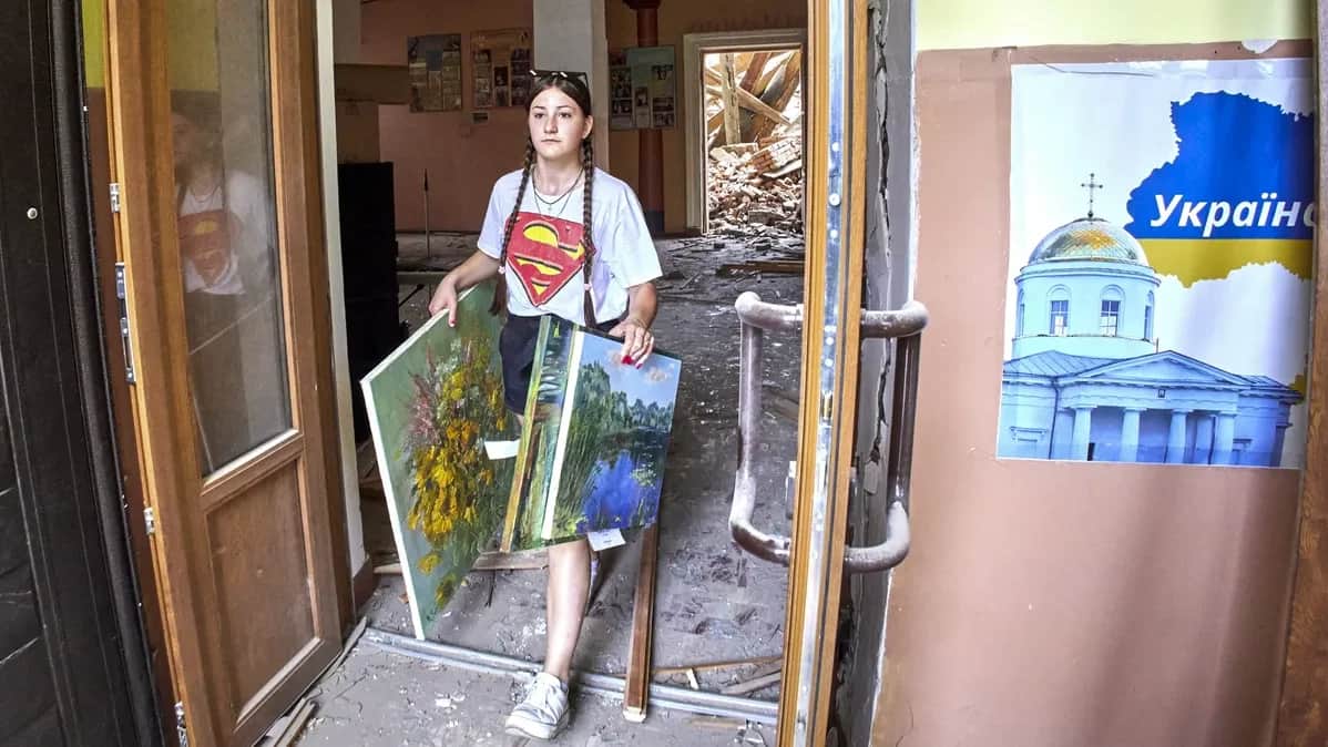 A girl carries paintings from the building of the socio-cultural center, which was damaged during the shelling in the city of Chuguev, Ukraine, on July 25, 2022. Photo by Sergey Kozlov / epa.eu