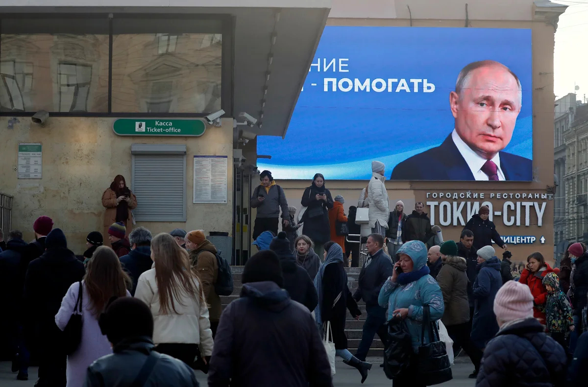 Прохожие на фоне большого экрана с изображением Путина в Санкт-Петербурге, 14 марта 2024 года. Фото: Анатолий Мальцев / EPA
