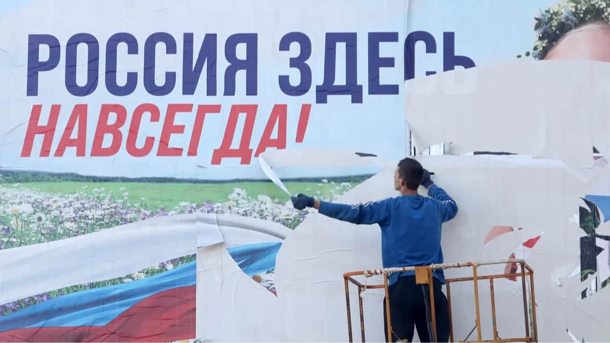 Рабочий срывает билборд с надписью «Россия здесь навсегда» в освобождённом от российской оккупации Херсоне, Украина, 14 ноября 2022 года. Фото: AFP / Scanpix / LETA