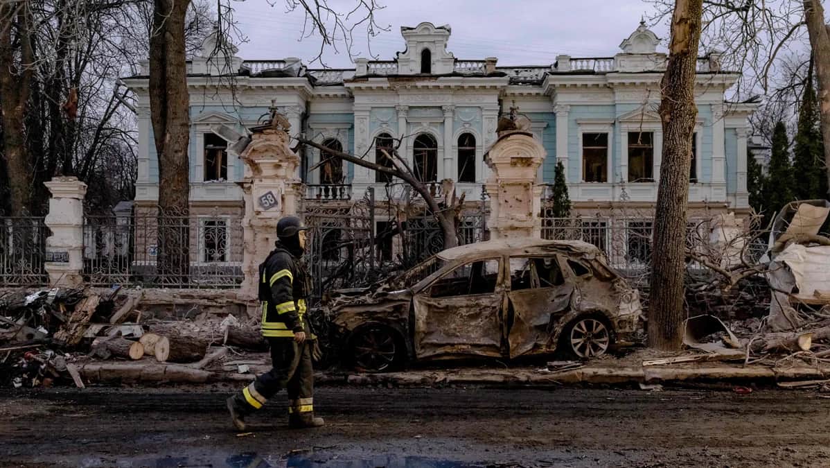 Спасатель проходит мимо сгоревшего автомобиля на фоне повреждённого здания после ракетного удара в Сумах, 13 апреля 2025 года. Фото: Roman Pilipey / AFP / Scanpix / LETA