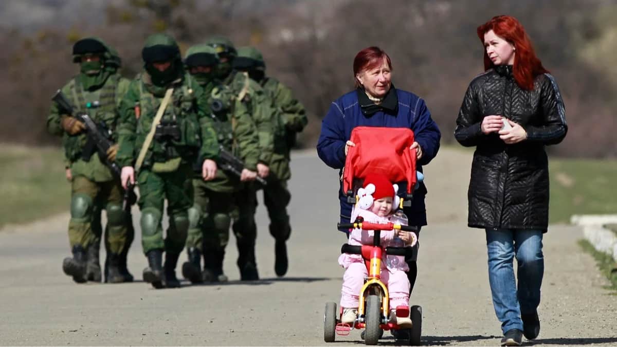 Местные жительницы проходят мимо вооруженных людей в военной форме без опознавательных знаков у входа в украинскую воинскую часть в селе Перевальное под Симферополем, 14 марта 2014 года. Фото: Юрий Кочетков / EPA<br>